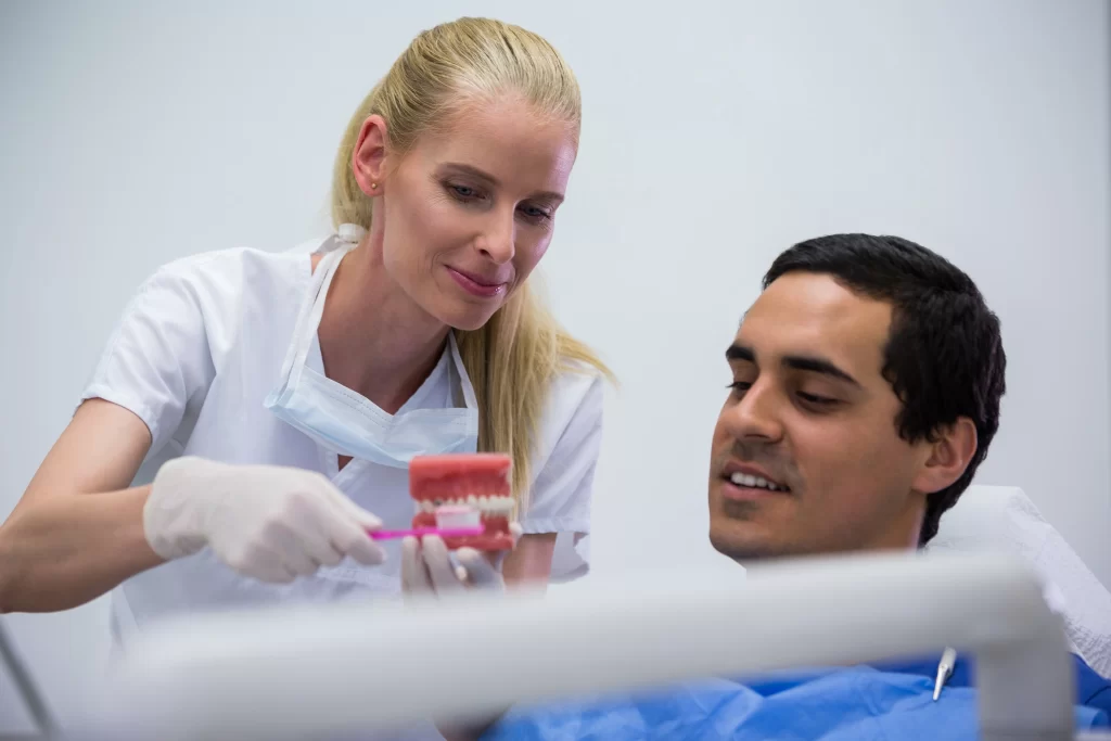 Dentist demonstrating proper dental implant care to a patient using a teeth model and toothbrush